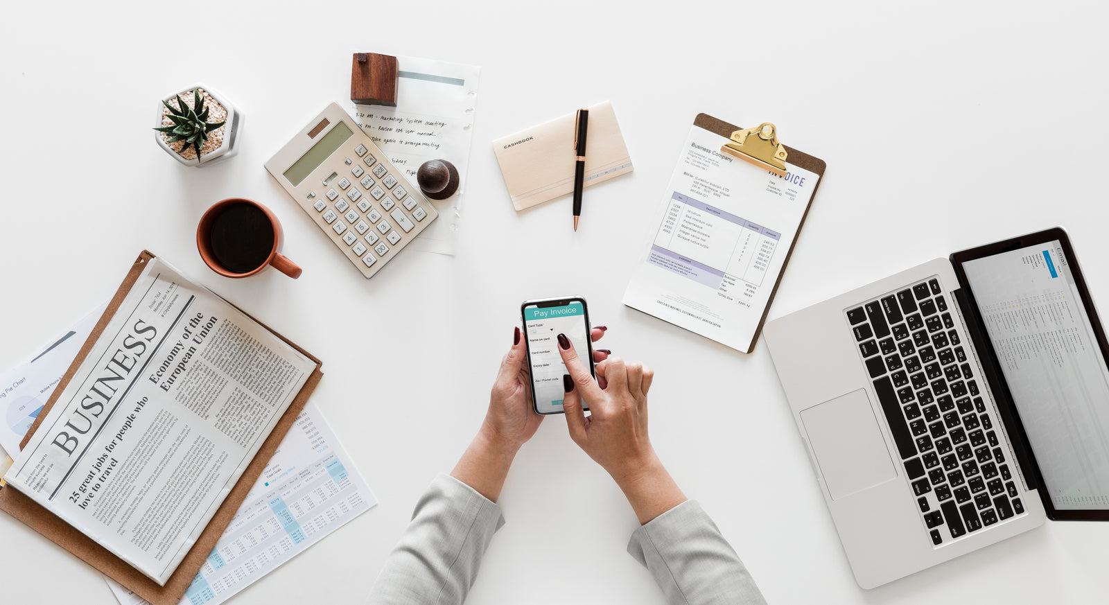 Overhead view of a desk with a phone, laptop, calculator and invoice