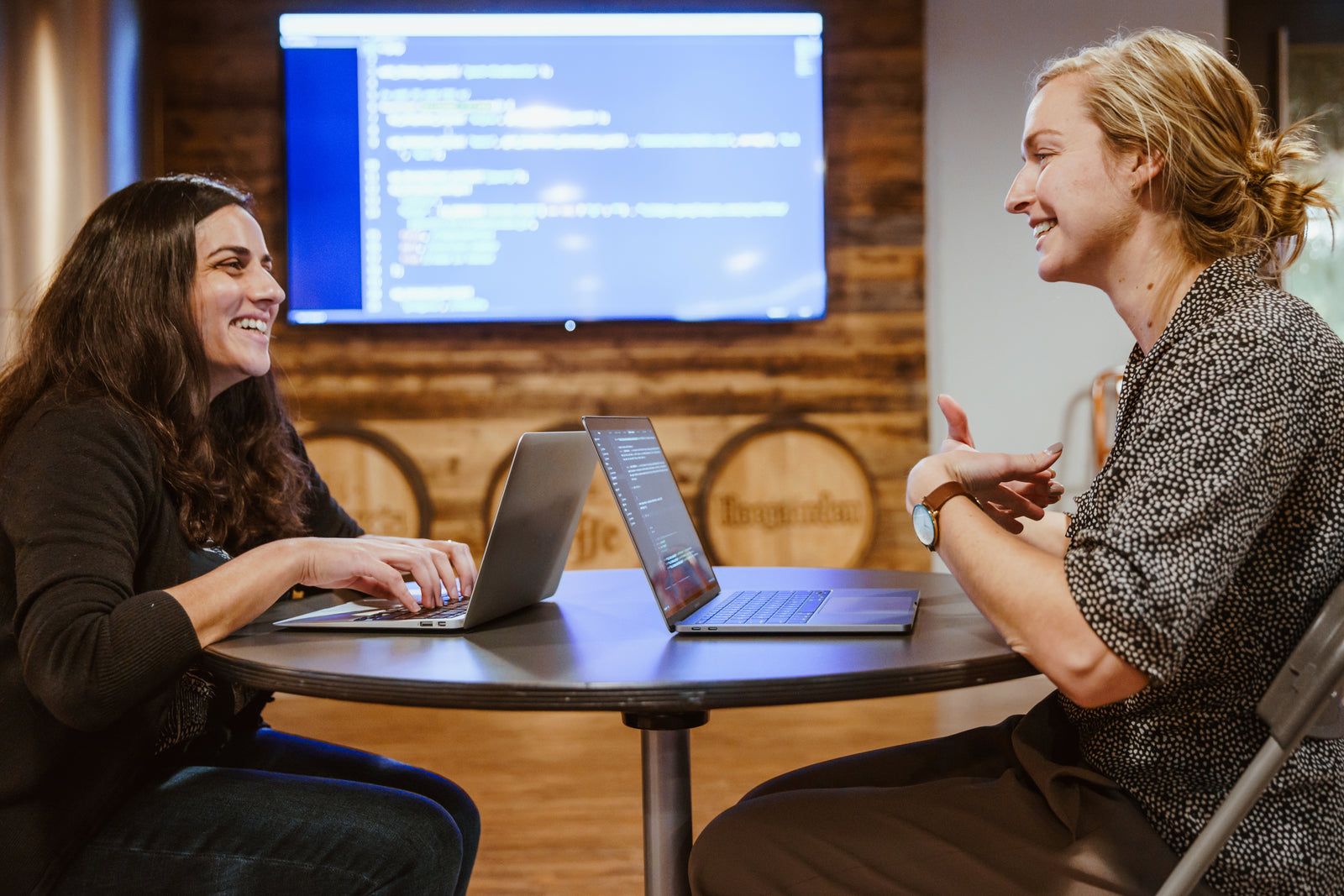 Two people smiling and talking over laptops at a table